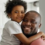 Pai abraçando sua filha criança, pois estão felizes com o que fazer no dia dos pais este ano