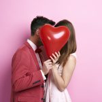 Casal de namorados segurando um coração e animado para fazer uma viagem no dia dos namorados