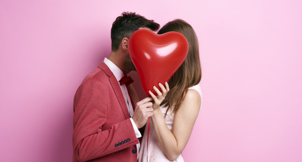 Casal de namorados segurando um coração e animado para fazer uma viagem no dia dos namorados